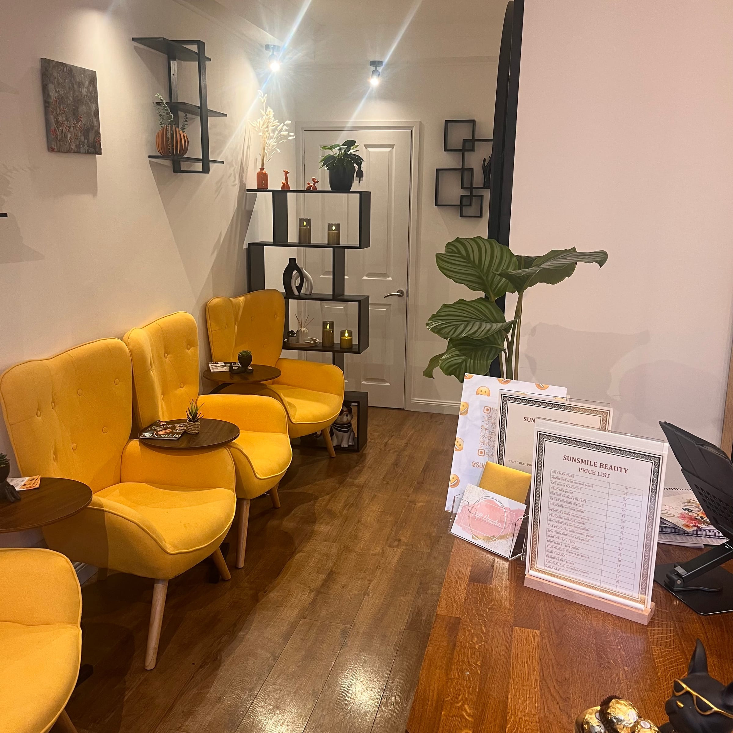 The Sunsmile waiting area — mustard tufted armchairs, dark wood floor, geometric wall shelves with candles and plants