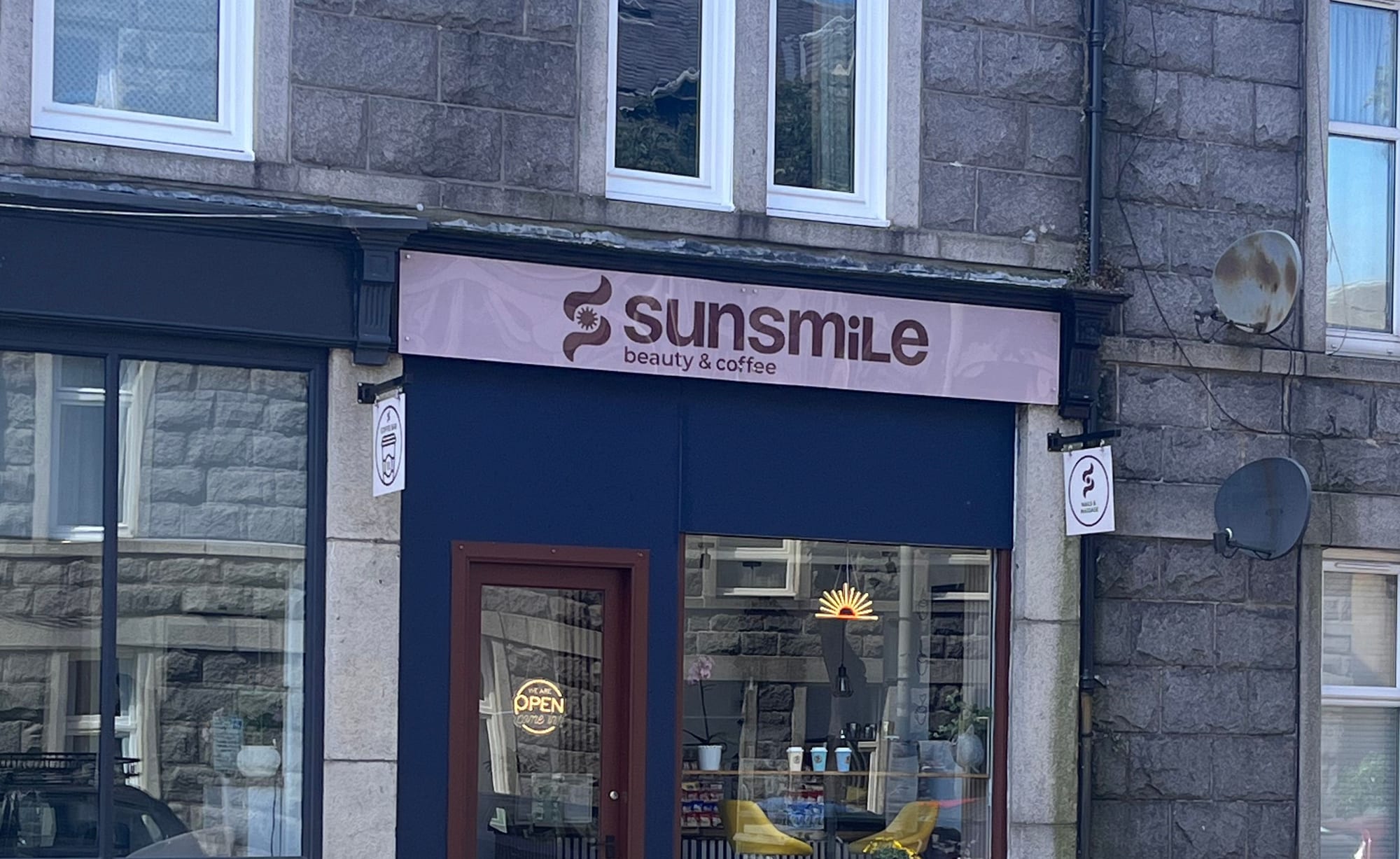 The Sunsmile shopfront on Great Western Place — pink sign reading Sunsmile beauty & coffee above a deep navy frontage, burgundy door and a neon sun in the window
